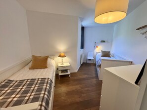 A narrow hotel room with a bed, bedside table, lamp, and a small desk with a chair. - Cozy apartment - 5 guests (Vars)