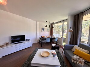A modern living room with a flat-screen TV, a dining area with a table set for two, and a sofa with a magazine. - Cozy apartment - 5 guests (Vars)