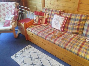 Ein hölzernes Bett mit Karo-Bettwäsche und Kissen, ein Sessel mit rotem Sitzkissen und ein gemustertes Teppich.
