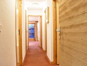 Un couloir avec des portes en bois et un sol recouvert de moquette, qui mène à un balcon offrant une vue panoramique.