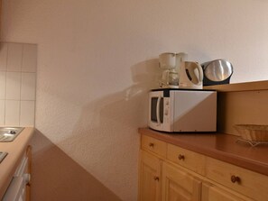 Une cuisine équipée d’un four à micro-ondes, d’une machine à café et d’une bouilloire, le tout posé sur le plan de travail.