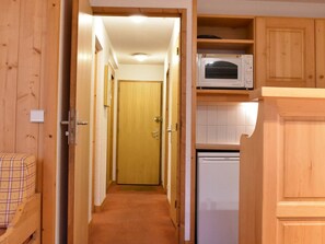 A narrow hallway with wooden walls and doors, leading to a room with a bed and a microwave above a white appliance. - Cozy apartment mountain view - 5 guests (Méribel)