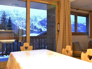 A room with a table and chairs, a window with a view of snow-covered mountains, and a wooden railing. - Cozy apartment mountain view - 5 guests (Méribel)