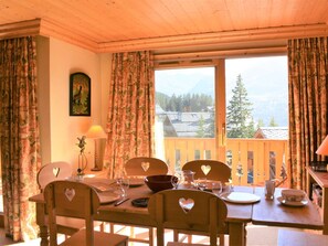 A dining area with wooden furniture, a table set for four, and a view of a mountain landscape through a window. - Ski-in apartment, valley view - 4 guests (Méribel)