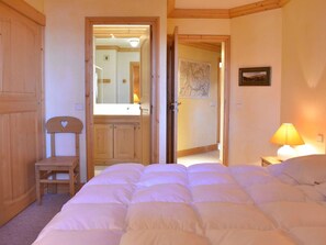 A bedroom with a bed, a chair, a nightstand with a lamp, and a door leading to another room. - Ski-in apartment, valley view - 4 guests (Méribel)