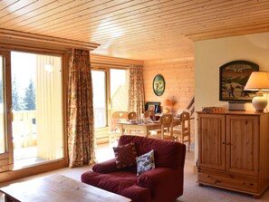 A cozy room with a wooden ceiling, a dining area with a table and chairs, a red sofa with a cushion, and a cabinet with a lamp. - Ski-in apartment, valley view - 4 guests (Méribel)