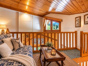 A cozy room with a bed, a wooden bench, a table with a candle, and a window with a view of a mountain landscape. - Spacious apartment, slopes view - 6 guests (Le Grand-Bornand)