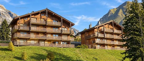 A wooden chalet-style hotel with multiple balconies, set against a mountainous backdrop.