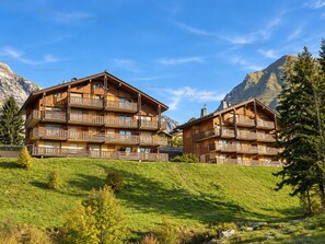 A wooden chalet-style hotel with multiple balconies, set against a mountainous backdrop. - Spacious apartment, slopes view - 6 guests (Le Grand-Bornand)