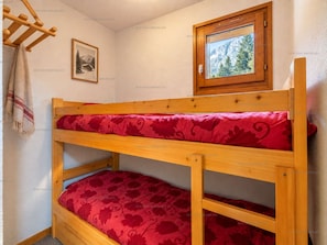 A bunk bed with a red patterned bedspread, a framed picture on the wall, and a window with a view of trees. - Spacious apartment, slopes view - 6 guests (Le Grand-Bornand)