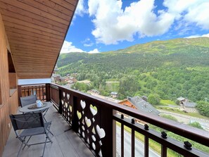 A balcony with a wooden railing and heart-shaped cutouts, overlooking a valley with houses and greenery. - Spacious apartment mountain view - 8 guests (Méribel)
