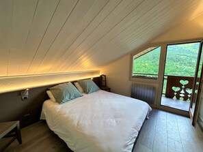 A bedroom with a bed, a nightstand, a window, and a view of greenery outside. - Spacious apartment mountain view - 8 guests (Méribel)