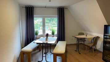 Un coin repas avec une table et des bancs, une petite fenêtre avec des rideaux et une vue sur la verdure à l’extérieur.