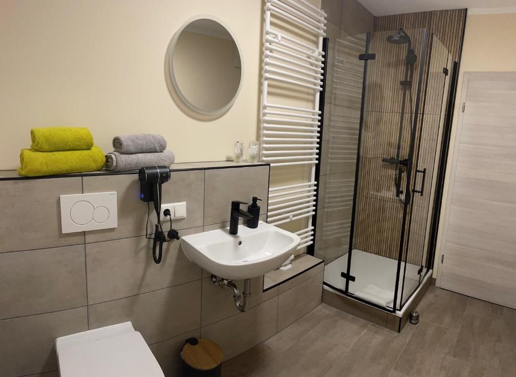 Une salle de bain avec un lavabo blanc, un miroir, un porte-serviettes avec des serviettes et une douche à parois de verre.