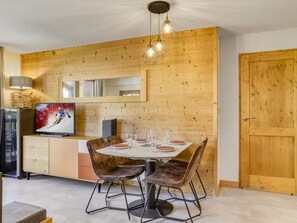 A dining area with a wooden wall, a TV, and a table set for four. - Apartment with wellness - 4 guests (Les Saisies)