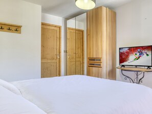 A hotel room with a bed, wooden wardrobe, a television on a small table, and a mirror on the wall. - Apartment with wellness - 4 guests (Les Saisies)