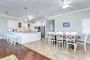 Une cuisine spacieuse dotée d’un îlot central, de tabourets de bar blancs, d’une table à manger avec des chaises et d’un ventilateur de plafond.