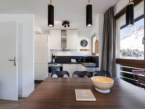A modern kitchen with a dining area, featuring a wooden table, chairs, and a view of snow-capped mountains through a window. - Modern cross-through apartment - 4-5 guests (Tignes-Val Claret)