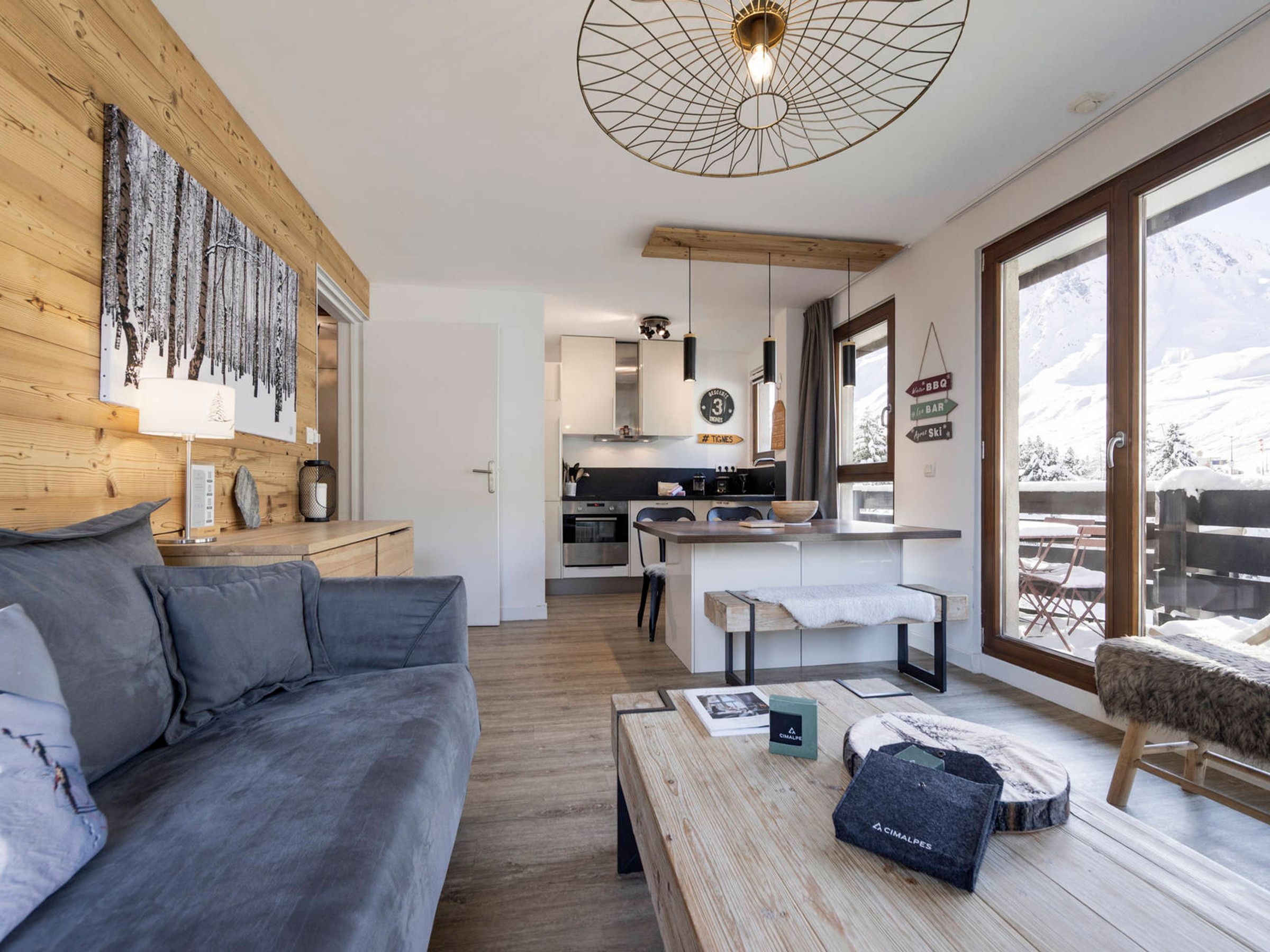 A modern living room with a grey sofa, wooden coffee table, and a view of a kitchen and dining area.