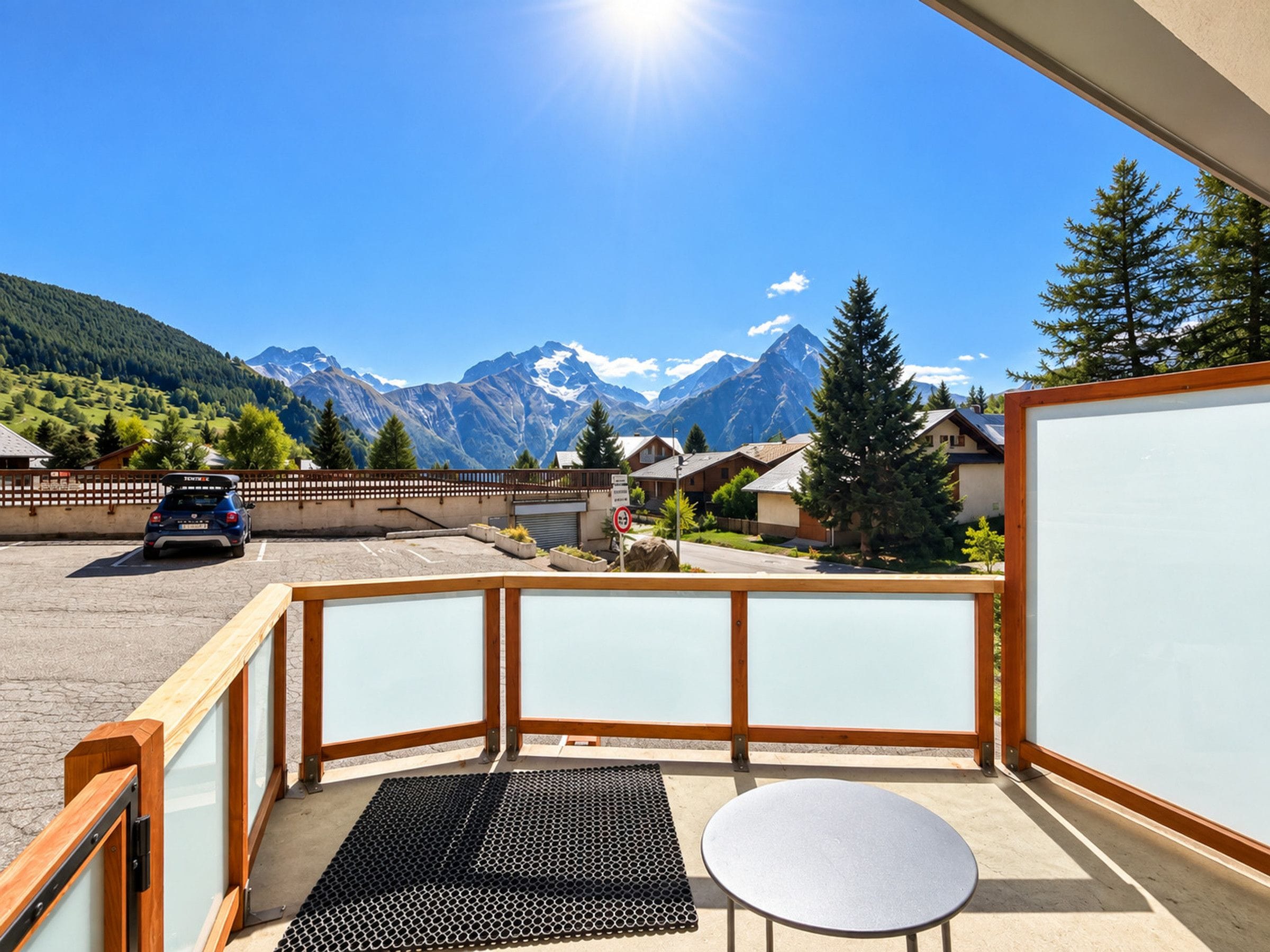 A balcony with a view of a mountain range, a parked car, and a small table.
