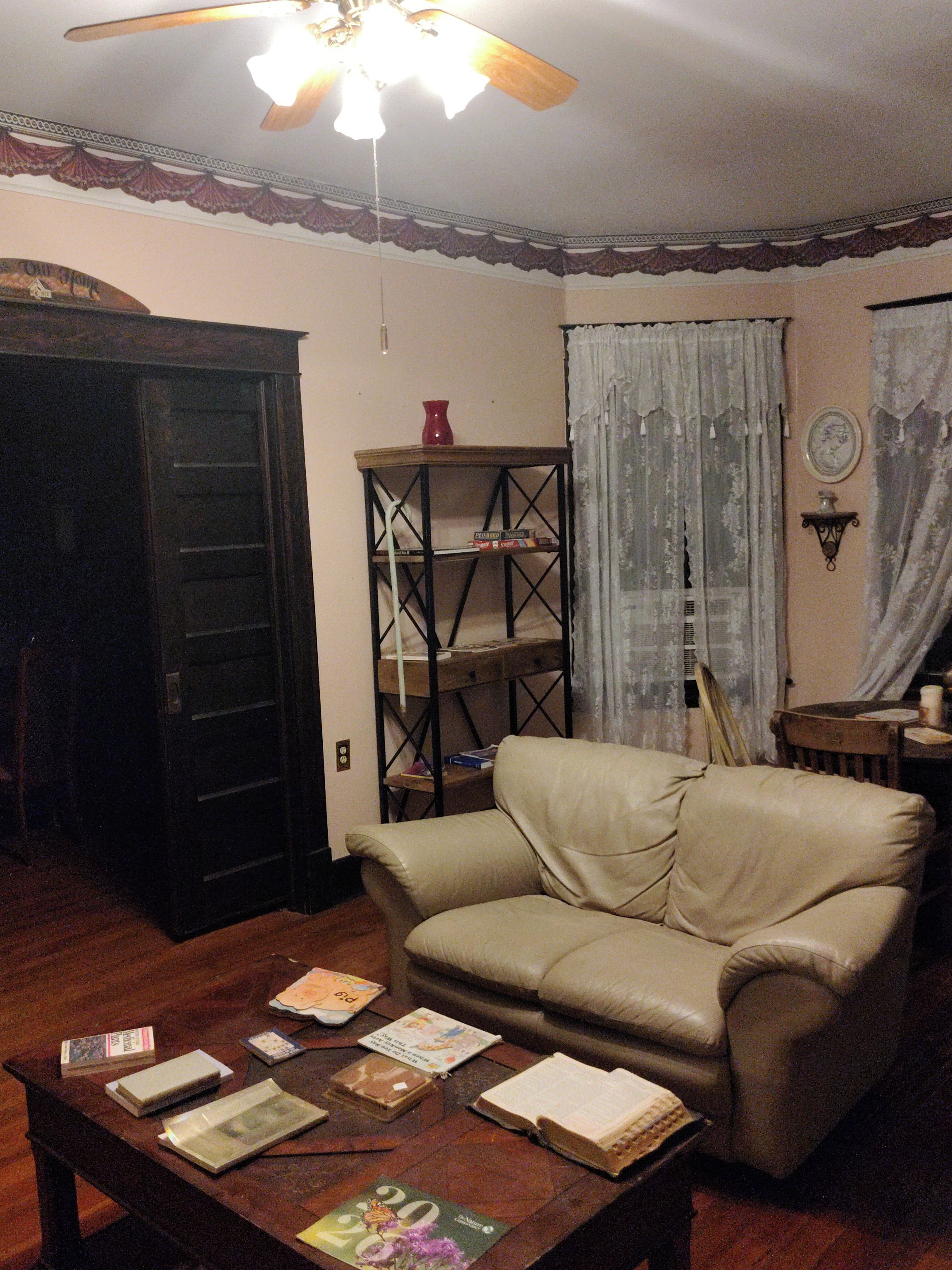 A living room with a leather sofa, a wooden coffee table with books, a bookshelf, and a ceiling fan.