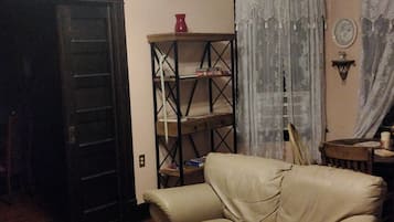 A living room with a leather sofa, a wooden coffee table with books, a bookshelf, and a ceiling fan.