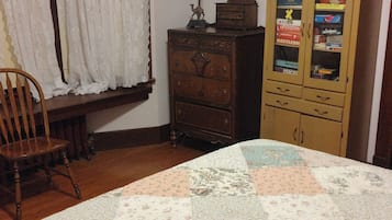 A room with a bed, a wooden cabinet with glass doors, a chair, and a window with curtains.