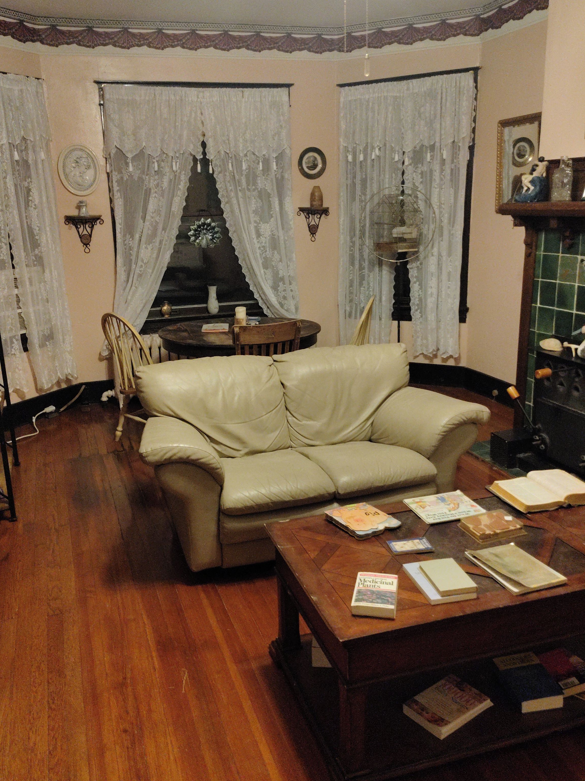 Ein Wohnzimmer mit einer Ledersofa, einem Couchtisch mit Büchern, einem Kamin und Spitze-Vorhängen.