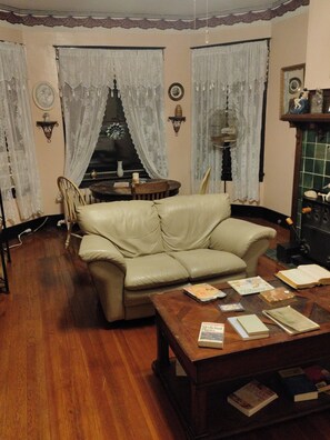 Una sala de estar con un sofá de cuero, una mesa de centro de madera con libros, una chimenea y cortinas de encaje.