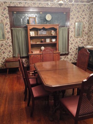 A dining room with a wooden table and chairs, a bookshelf, and a clock on the wall.