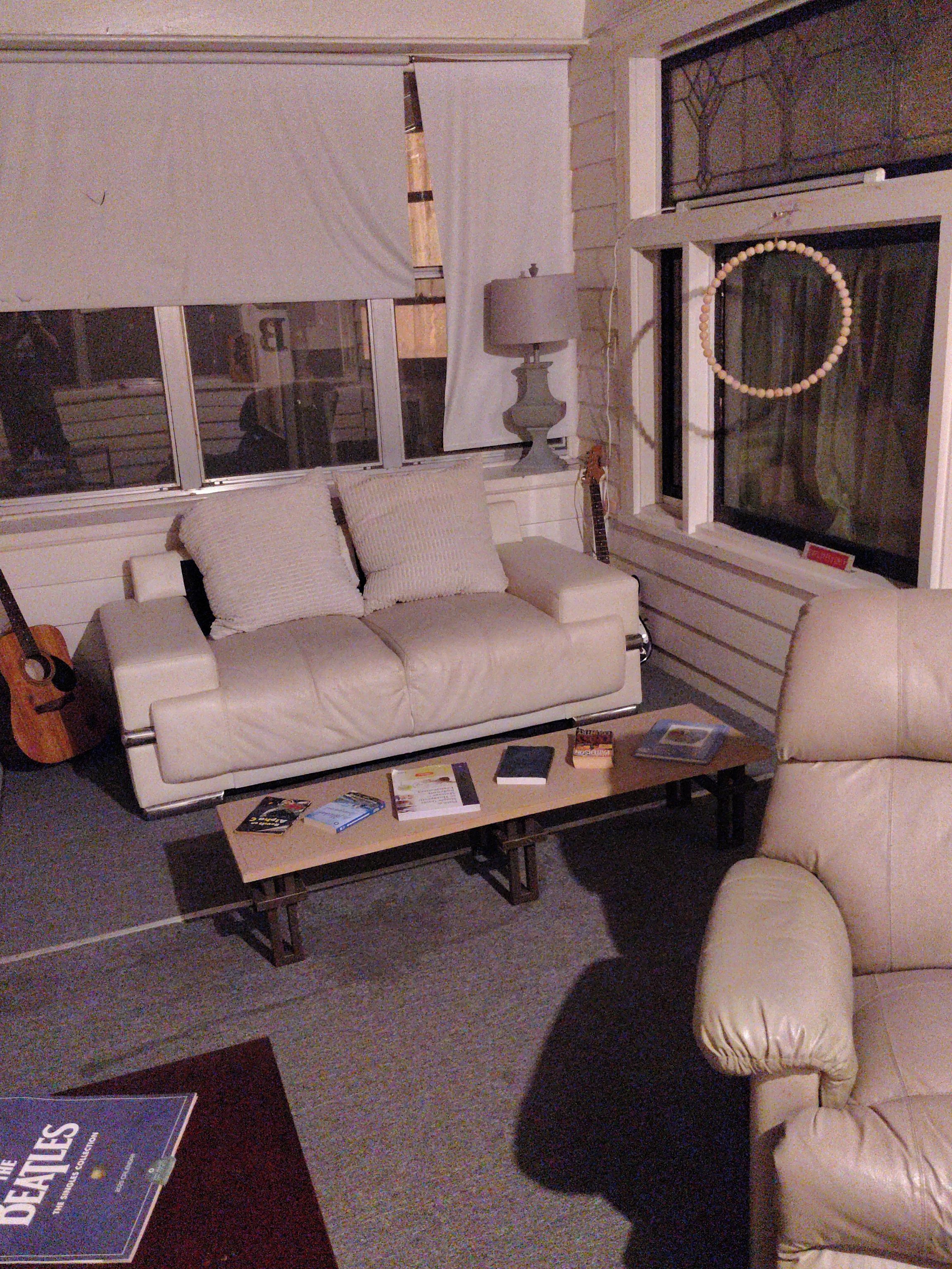 A living room with a sofa, a coffee table with books, a guitar, and a lamp.