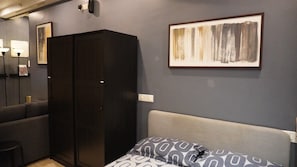 A bedroom with a bed, a wardrobe, a wall-mounted light, and a framed abstract painting. - London Studio I Hiranandani Estate I WiFi (Thane)
