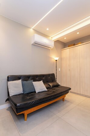 Una sala de estar moderna con un sofá de cuero negro, cojines estampados, una lámpara de pie y un armario de madera.
