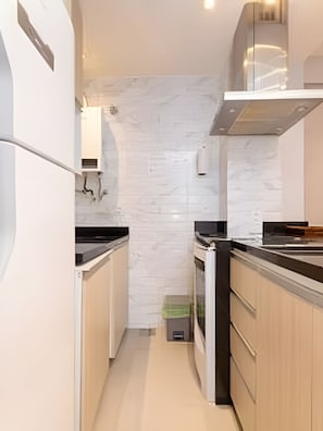 A narrow kitchen with white cabinets, a black countertop, and a stainless steel range hood. - Edifício Master - Apt 3 minutos da praia (Rio de Janeiro)
