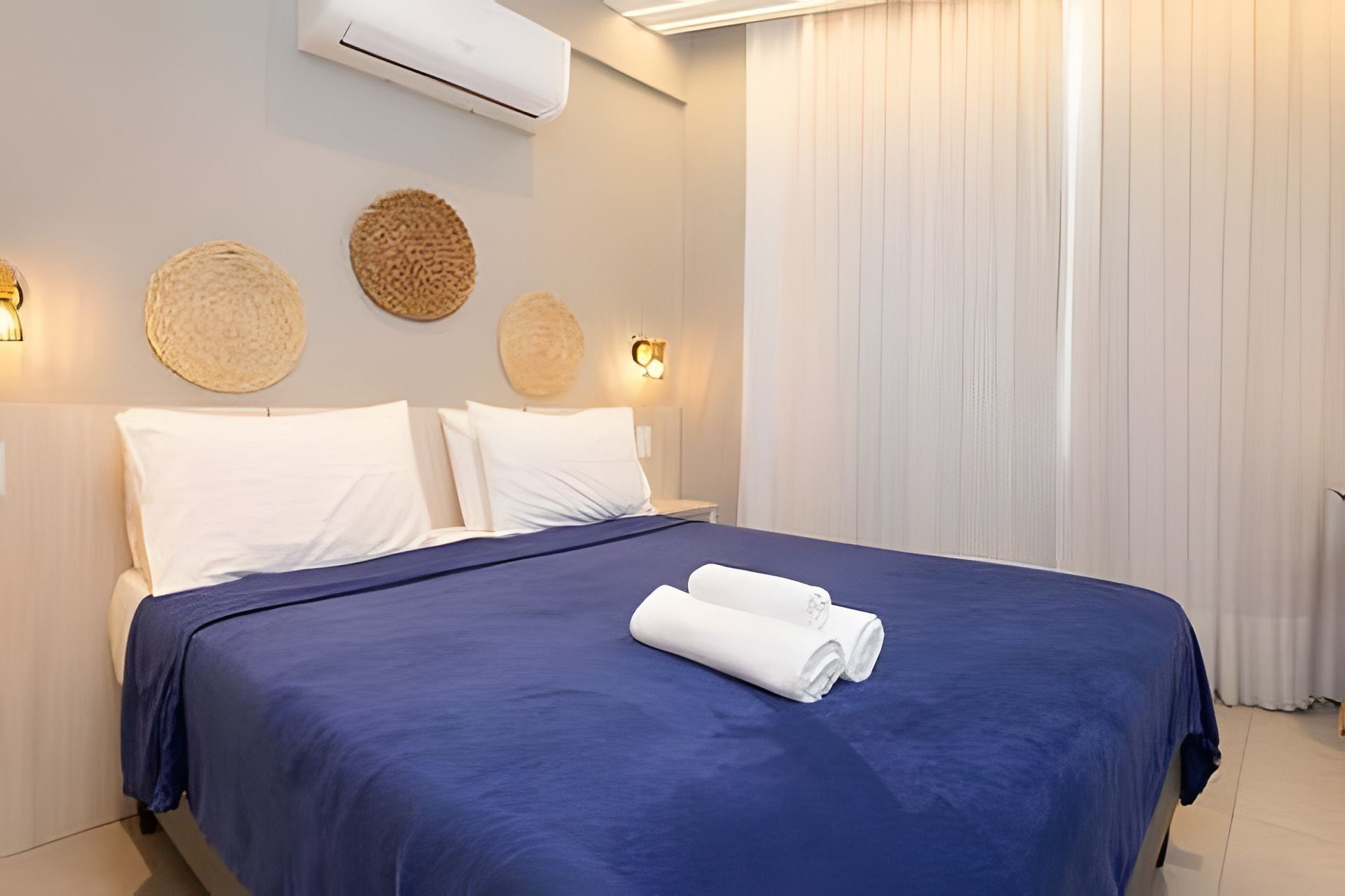 A hotel room with a large bed, two pillows, a blue bedspread, and two wall-mounted lamps.