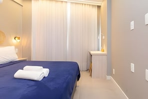 A hotel room with a bed, a nightstand, a mirror, and a window with curtains. - Edifício Master - Apt 3 minutos da praia (Rio de Janeiro)