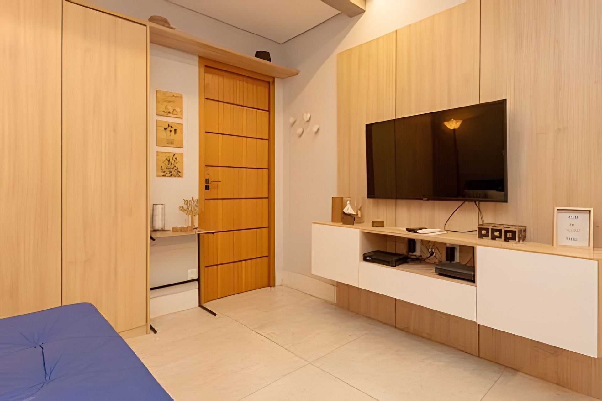 A modern room with a television mounted on a wooden cabinet, a sliding door closet, and a small shelf with decorative items.