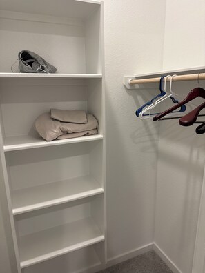 Ein weißer Kleiderschrank mit Regalen und einer Kleiderstange, außerdem ein Paar Schuhe auf der obersten Ablagefläche.