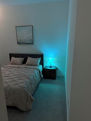 Ein Schlafzimmer mit einem Bett, einem Nachttisch, einer Lampe und einem Bild an der Wand.