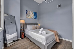 Ein Schlafzimmer mit einem Bett, einem Nachttisch, einer Lampe, einem Spiegel und einem Bild an der Wand.
