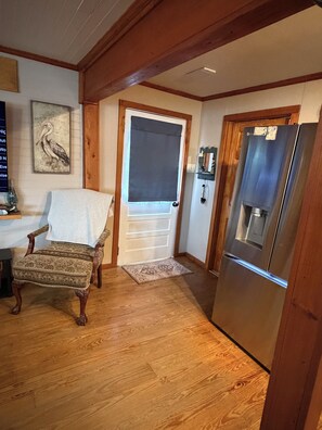 A wooden-framed room with a door, a chair, a refrigerator, and a patterned rug. - The Fisherman’s Hideaway (Vacherie)