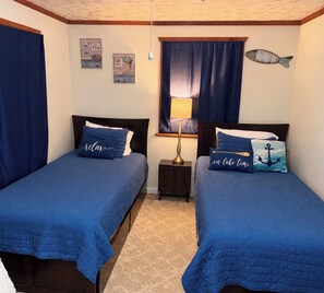 A room with two beds, each with a blue bedspread and matching pillows, a small bedside table with a lamp, and a wall decoration of a fish. - The Fisherman’s Hideaway (Vacherie)