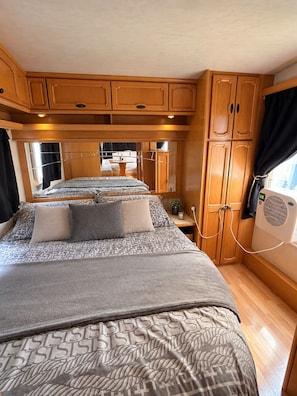 A compact RV bedroom with a bunk bed, wooden cabinets, and a small table with a plant. - A Unique Getaway & Spa Experience Between Chartres, Orléans, and Paris. (Orgères-en-Beauce)