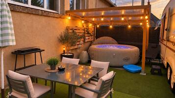 An outdoor patio with a table and chairs, a hot tub, and a pergola with string lights.