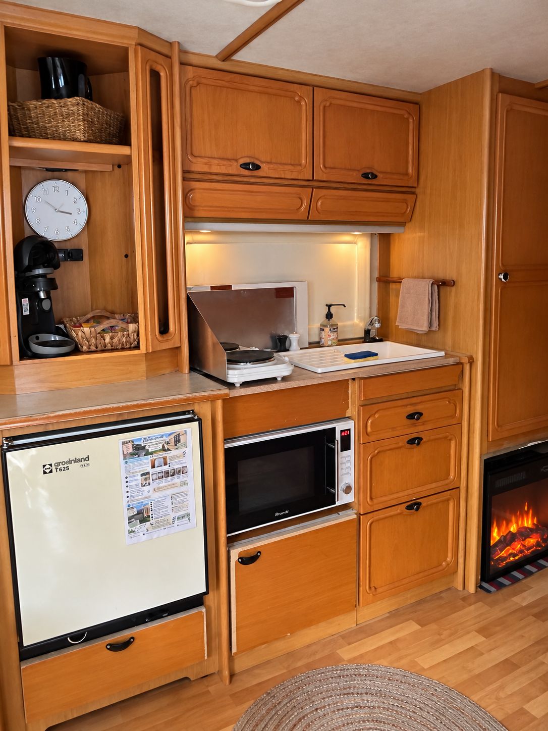 Een kleine keuken met een koelkast, magnetron, koffiezetapparaat en een eethoekje.