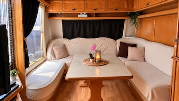Een gezellig interieur van een camper, met een zachte zithoek, een klein tafeltje met een kaars en een raam met gordijnen.