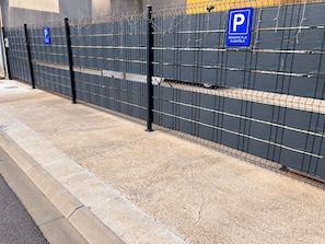 A parking area with a metal fence and a blue parking sign. - A unique wellness experience between Chartres, Orléans, and Paris. (Orgères-en-Beauce)