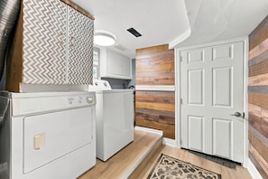 A laundry room with a washing machine, dryer, and a door leading to another room. - Historic Toronto Cottage with Small-Town Charm steps to GO & Subway SIMZEN T.O. (Toronto)
