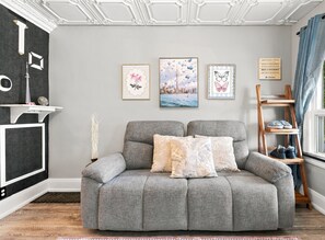A grey sofa with patterned cushions, a decorative wall with framed artwork, and a wooden shoe rack by a window. - Historic Toronto Cottage with Small-Town Charm steps to GO & Subway SIMZEN T.O. (Toronto)