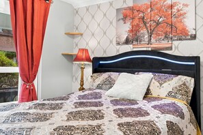 A bed with patterned bedding, a red lamp, and a wall with a tree painting. - Historic Toronto Cottage with Small-Town Charm steps to GO & Subway SIMZEN T.O. (Toronto)